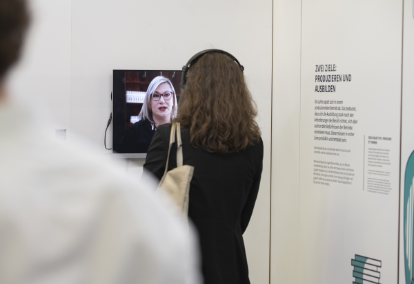Une femme avec des écouteurs se tient devant un écran de l'exposition «Au cœur de l’apprentissage»