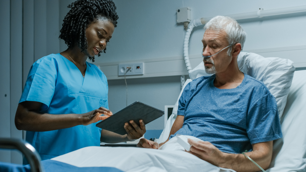 Une infirmière munie d'une tablette électronique parle à un patient âgé à l'hôpital.