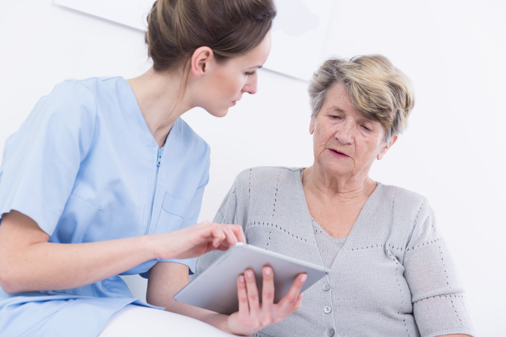 une infirmière explique quelque chose à une senior via un dispositif numérique