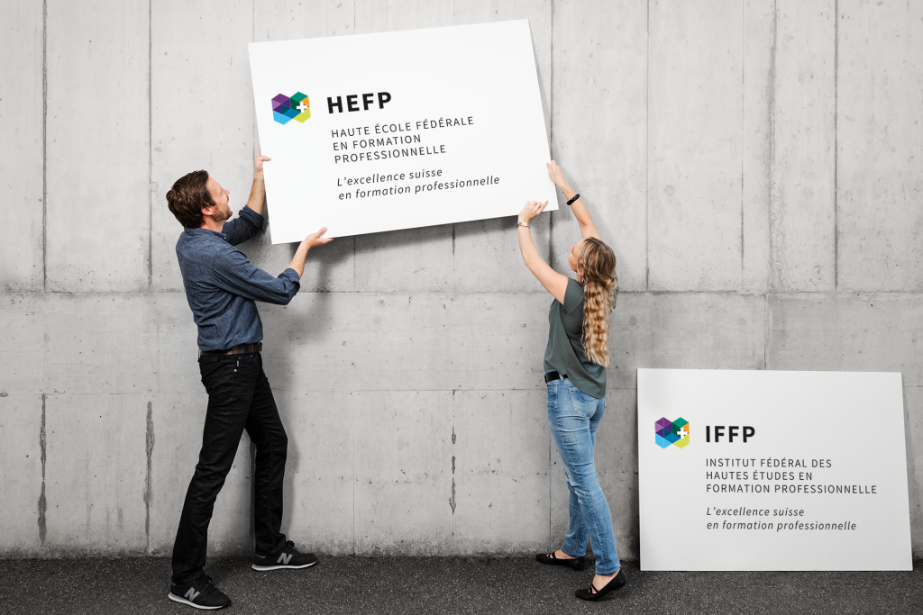 Un homme et une femme brandissent un panneau portant le nouveau nom de la Haute école fédérale en formation professionnelle HEFP 