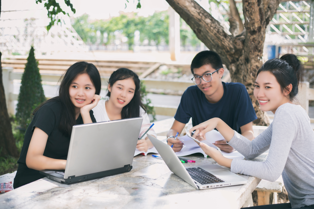 Groupe d'étudiants asiatiques utilisant une tablette et un ordinateur portable et partageant leurs idées pour travailler sur la pelouse du campus.