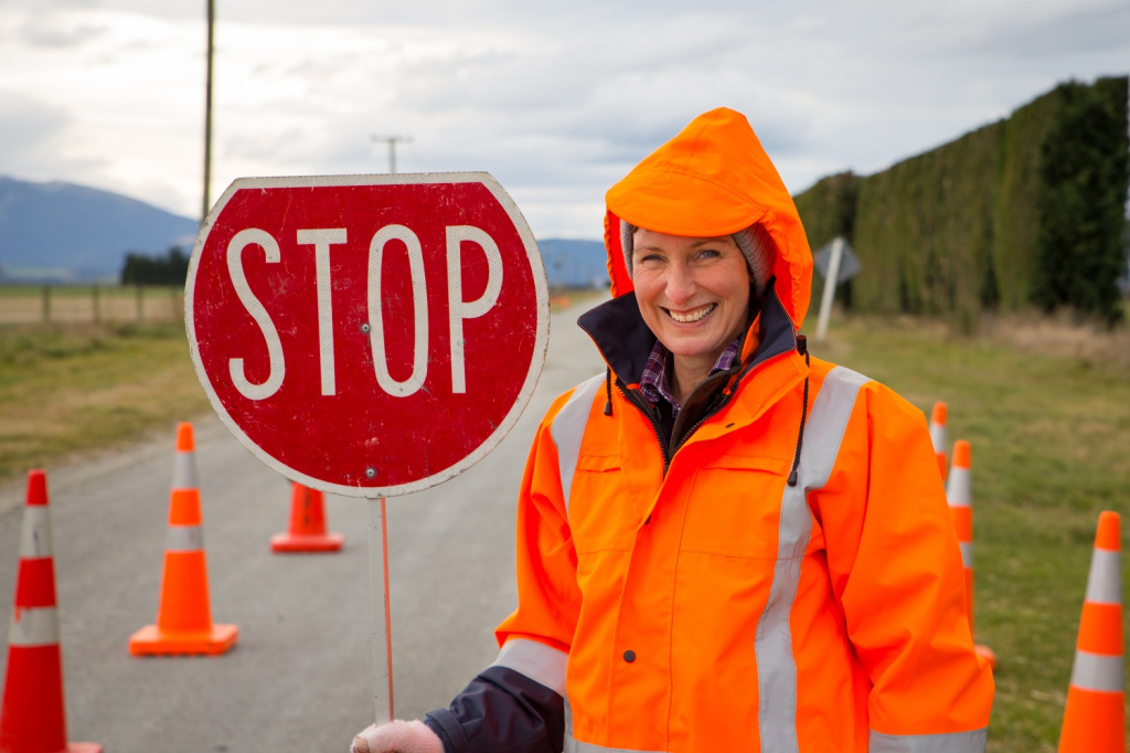 Une femme faisant partie d'une équipe de voirie actionne un panneau d'arrêt à un endroit dangereux sur une route rurale à Canterbury, en Nouvelle-Zélande.